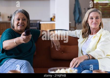 A casa, guardando la TV, due donne anziane si rilassano sul divano e si divertono insieme Foto Stock