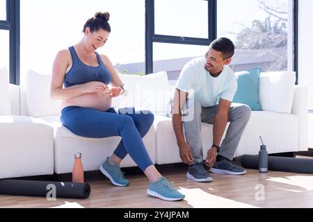 A casa, coppia multirazziale, donna incinta e uomo che si preparano per l'allenamento con tappetini da yoga Foto Stock