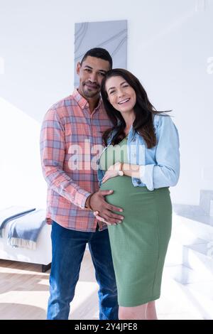 A casa, coppia multirazziale, donna incinta sorridente con partner, entrambe con la pancia Foto Stock