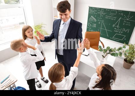 Insegnante di sesso maschile che dà alti voti ai piccoli alunni in classe Foto Stock