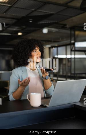 Parla con uno smartphone, una donna che lavora con un computer portatile con una tazza da caffè in ufficio Foto Stock
