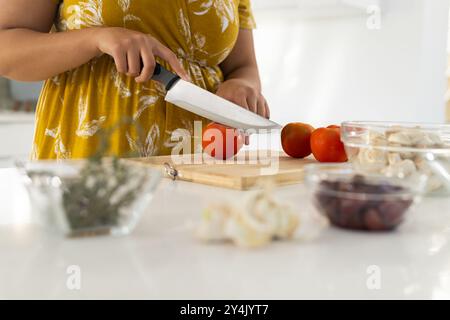 Tritare i pomodori sul tagliere, donna con capelli ricci che prepara gli ingredienti in cucina Foto Stock