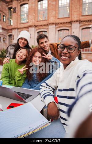 Verticale. Una studentessa afroamericana che fa un selfie con i suoi amici usando uno smartphone. Gruppo di compagni di classe multirazziali che fanno un ritratto con un cellulare alla riunione del campus universitario. Foto di alta qualità Foto Stock