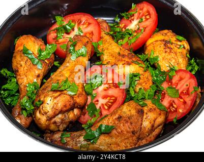 Gustosi cosce di pollo cotte con pomodori e verdure in una profonda teglia nera. Foto Stock