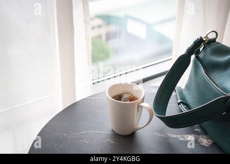 Tazza di tè caldo e borsa accanto alle finestre con tende bianche. Copia spazio. Foto Stock