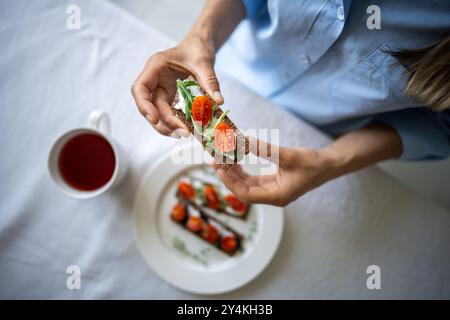 Mani femminili che tengono il panino con cura, dall'alto sopra la vista, focalizzazione morbida sulle braccia della donna con toast. Foto Stock