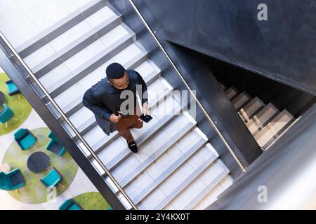 Salendo le scale, un uomo d'affari che tiene in mano smartphone e tazza di caffè nell'edificio degli uffici Foto Stock