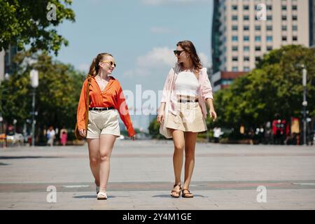 Due donne che camminano lungo City Street alla luce del giorno Foto Stock