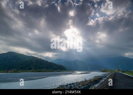Un drammatico gioco di luci e ombre si svolge su una valle del fiume. La luce del sole attraversa a intermittenza un baldacchino di nuvole, gettando fasci di ligine Foto Stock