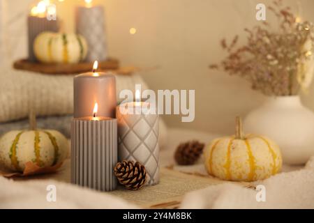 Candele, zucche e coni bruciati vicino alla parete beige. Atmosfera autunnale Foto Stock