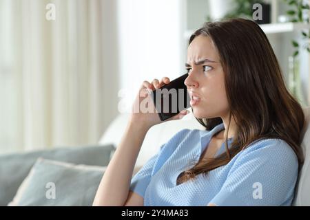 Donna disgustata che parla al telefono seduto su un divano a casa Foto Stock