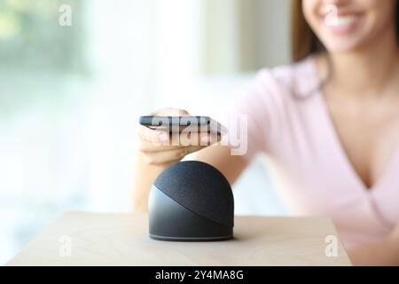 Primo piano di una donna felice che abbina l'altoparlante intelligente al telefono cellulare di casa Foto Stock