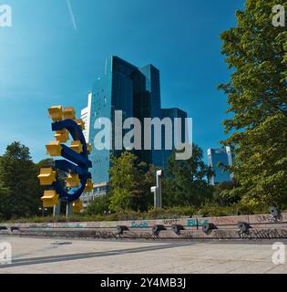 Francoforte, Hess, Germania - 2024, 23 luglio: Il grande simbolo dell'euro a Francoforte con vista sul parco e un grande grattacielo sullo sfondo preso da Be Foto Stock