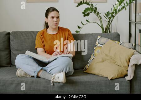 Giovane donna seria che legge il libro in Braille mentre trascorre del tempo a casa Foto Stock