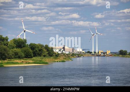 Turbine eoliche vicino al fiume Elba a Magdeburgo, circondate da alberi e strutture industriali sotto il cielo nuvoloso. Foto Stock