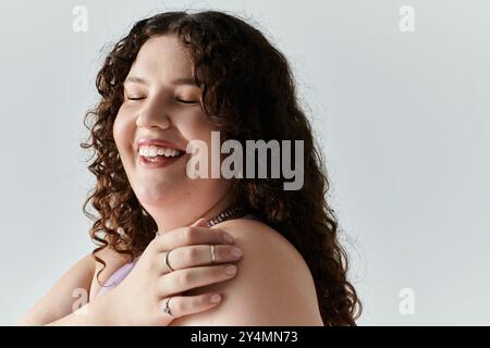 Una donna graziosa e di grandi dimensioni irradia felicità toccando giocosamente le spalle con un sorriso gentile. Foto Stock