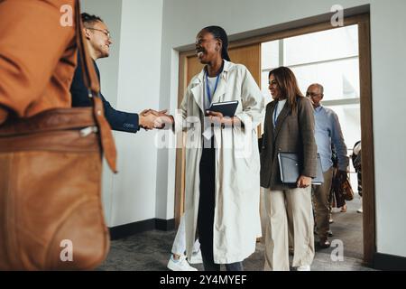 Workshop aziendale con un gruppo eterogeneo di professionisti che stringono la mano, discutono di formazione e networking. Foto Stock
