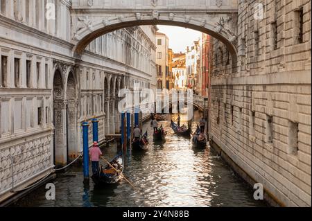 Vista posteriore dei gondolieri maschi che regnano lunghe e strette barche e attraversano il Ponte dei Sospiri tra gli edifici della città di Venezia Foto Stock