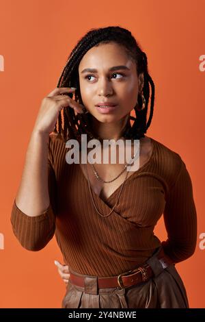 Una giovane donna afroamericana mette in mostra il suo stile con capelli intrecciati, in un vivace ambiente da studio. Foto Stock