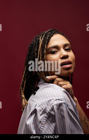 Una giovane ed elegante donna afroamericana sfoggia la sua acconciatura intrecciata in un elegante ambiente da studio. Foto Stock