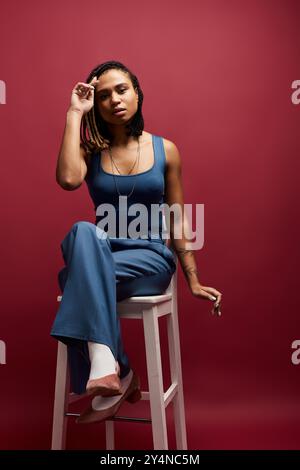 Una giovane donna afroamericana con i capelli intrecciati mostra il suo stile mentre è seduta in uno studio. Foto Stock