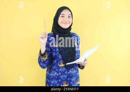 Giovane donna Hijab ASN lavoratrice governativa che indossa l'uniforme Korpri Batik tenendo una matita, controllando la carta di documenti Foto Stock