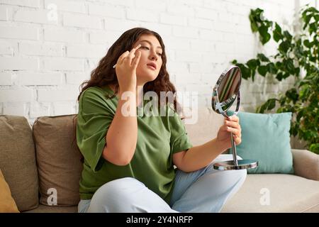 Una giovane donna di grandi dimensioni applica il trucco nel suo soggiorno, circondato da prodotti di bellezza e uno specchio. Foto Stock