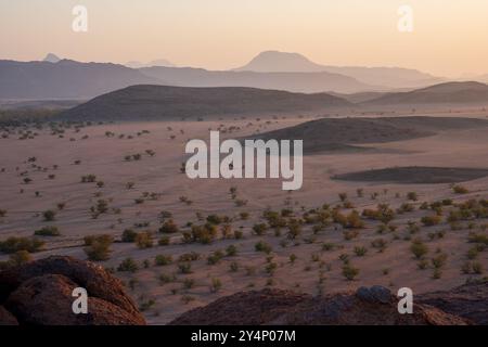 Una vista attraverso le montagne e il deserto di Twyfelfontein, Namibia, mostrando gli strati di terreno nella foschia mentre il sole tramonta Foto Stock