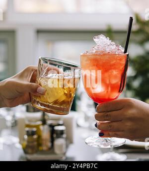 Gli amici brindano con bicchieri di whisky e cocktail di fragole Foto Stock