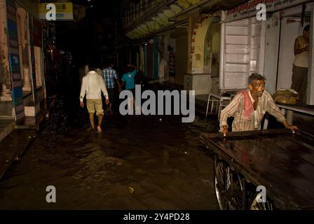 Piogge monsoniche, pellegrini e rituali di cremazione lungo il fiume Gange sono visti nella città Santa di Varanasi in India Foto Stock