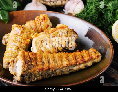 Pezzi di pesce cotti e fritti su un piatto di ceramica Foto Stock