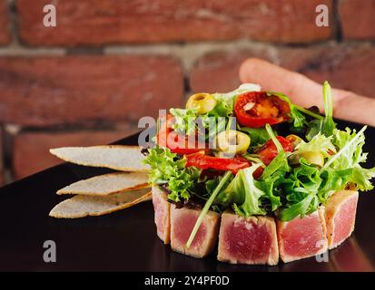 tartare di tonno servita con pane tostato e insalata su un piatto di pietra nera Foto Stock