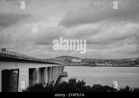 Dundee Scozia: 4 agosto 2024: Il Tay Bridge si estende su un calmo corpo d'acqua con un cielo nuvoloso sopra in un paesaggio urbano Foto Stock