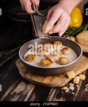 donna che grattugia il parmigiano sulle polpette in salsa panna Foto Stock