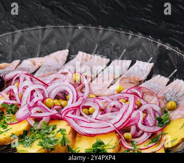 Fettine di aringhe con patate al forno e cipolle marinate su un piatto di vetro Foto Stock