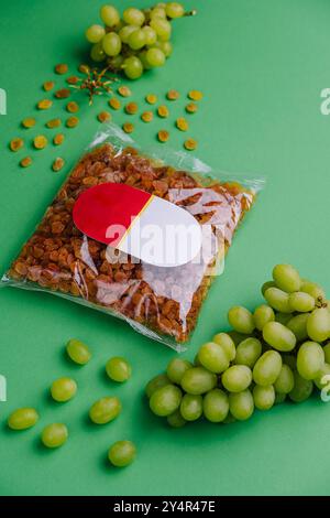uva passa confezionata e uva su sfondo verde Foto Stock