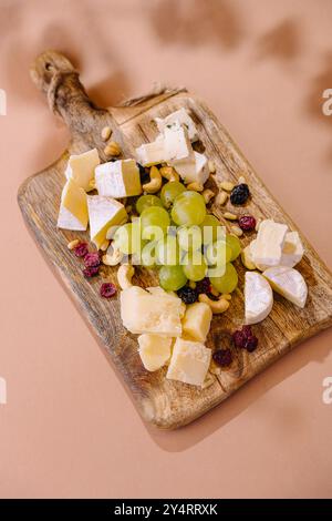 Selezione di formaggi e uve pregiati disposti su un tagliere rustico con fondo rosa Foto Stock