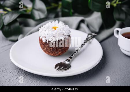 Squisito dessert al cocco su un piatto bianco guarnito con scaglie di cocco, abbinato a un tè Foto Stock