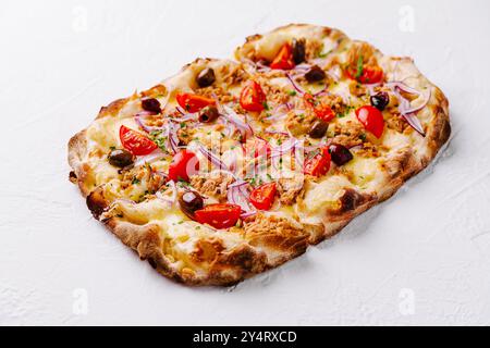 Pizza appena sfornata con tonno, pomodoro, olive e cipolle su una superficie bianca croccante Foto Stock