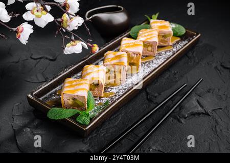 Eleganti sushi Rolls con kiwi e banana serviti su un piatto con un ramo sakura, su uno sfondo di pietra scura Foto Stock