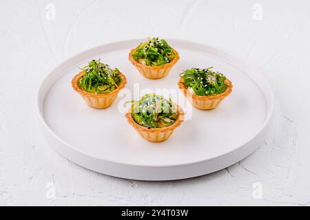 Antipasto elegante, insalata di alghe in conchiglie crostate, servita su un piatto bianco moderno Foto Stock