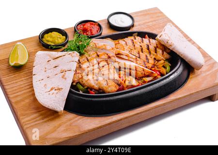 Gustose fajitas di pollo alla griglia servite con tortillas e salse da immersione su un tavolo di legno Foto Stock