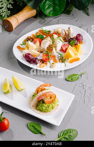 Elegante disposizione di antipasti di gamberi e un piatto di formaggi con noci e frutta su un tavolo moderno Foto Stock