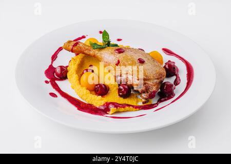 Elegante presentazione di anatra confit su un letto di purea cremosa con vivace salsa di frutti di bosco Foto Stock