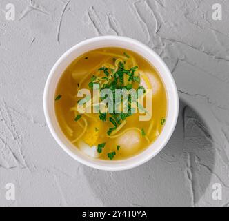 Vista dall'alto di una ciotola di zuppa di spaghetti di pollo fresca guarnita con prezzemolo su sfondo grigio Foto Stock