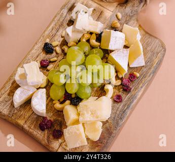 Selezione di formaggi e uve pregiati disposti su un tagliere rustico con fondo rosa Foto Stock