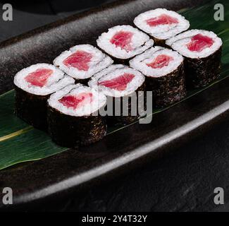 Sushi roll di tonno ben organizzato, su una foglia, con zenzero e wasabi, su un'elegante superficie nera Foto Stock