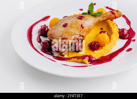 Elegante presentazione di anatra confit su un letto di purea cremosa con vivace salsa di frutti di bosco Foto Stock