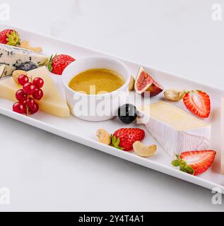 Elegante selezione di formaggi serviti con frutti di bosco freschi, fichi e salsa da immersione su un piatto bianco e sullo sfondo di marmo Foto Stock