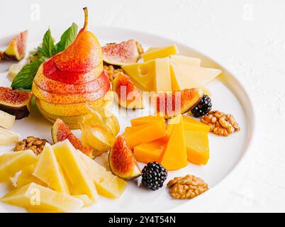 Elegante disposizione di vari formaggi, fichi freschi, pera e noci su un piatto di ceramica Foto Stock